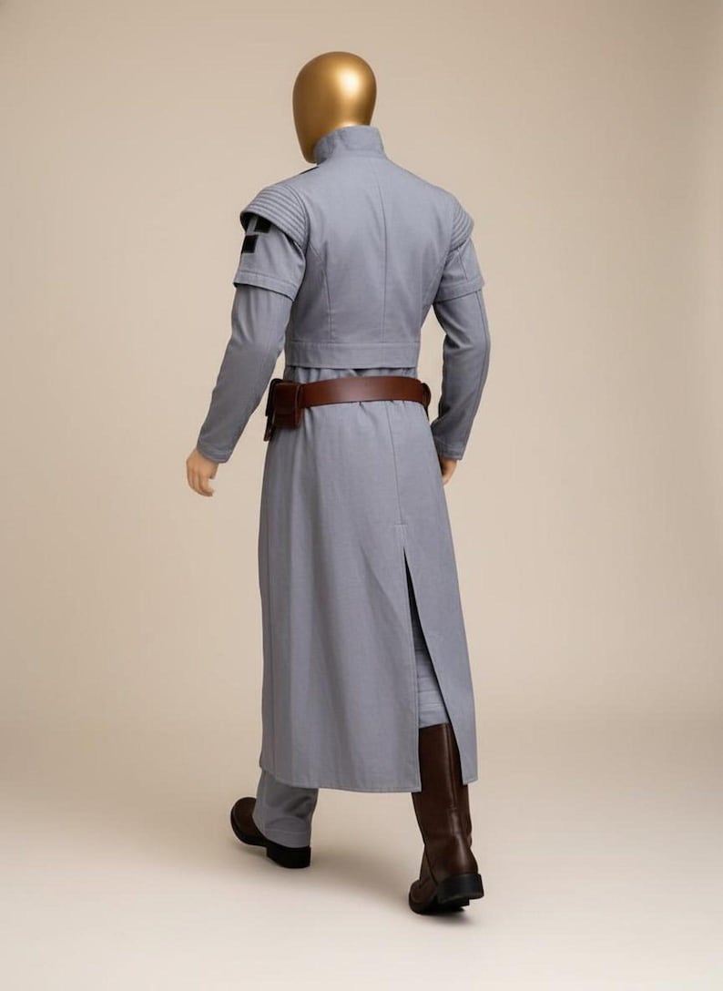 May include: A light gray costume with a high collar, long sleeves, and a long coat. The costume includes a brown belt and boots. The mannequin has a gold head. The costume is a sci-fi or fantasy style.