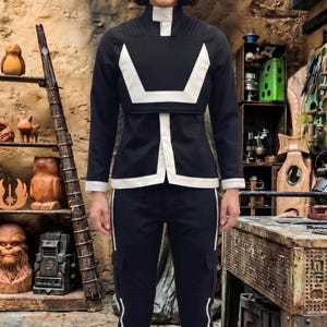May include: A black long-sleeved jacket with a high collar and white trim, paired with matching black cargo pants featuring white side stripes. The jacket has a structured white panel across the chest and white cuffs, creating a uniform appearance.