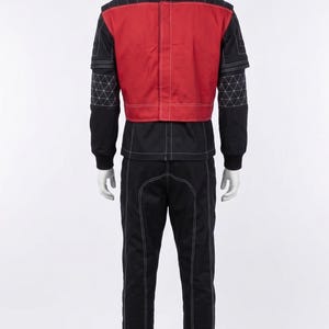 May include: A black and red jumpsuit featuring a high collar, long sleeves with white geometric grid stitching, and a solid red back panel. The garment includes white contrast stitching throughout, a full-length back zipper, and long black trousers.