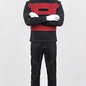 May include: A black long-sleeved shirt with a high collar and a red chest panel featuring a rectangular black patch. The shirt has white contrast stitching throughout. Matching black trousers with white contrast stitching are worn with the shirt.