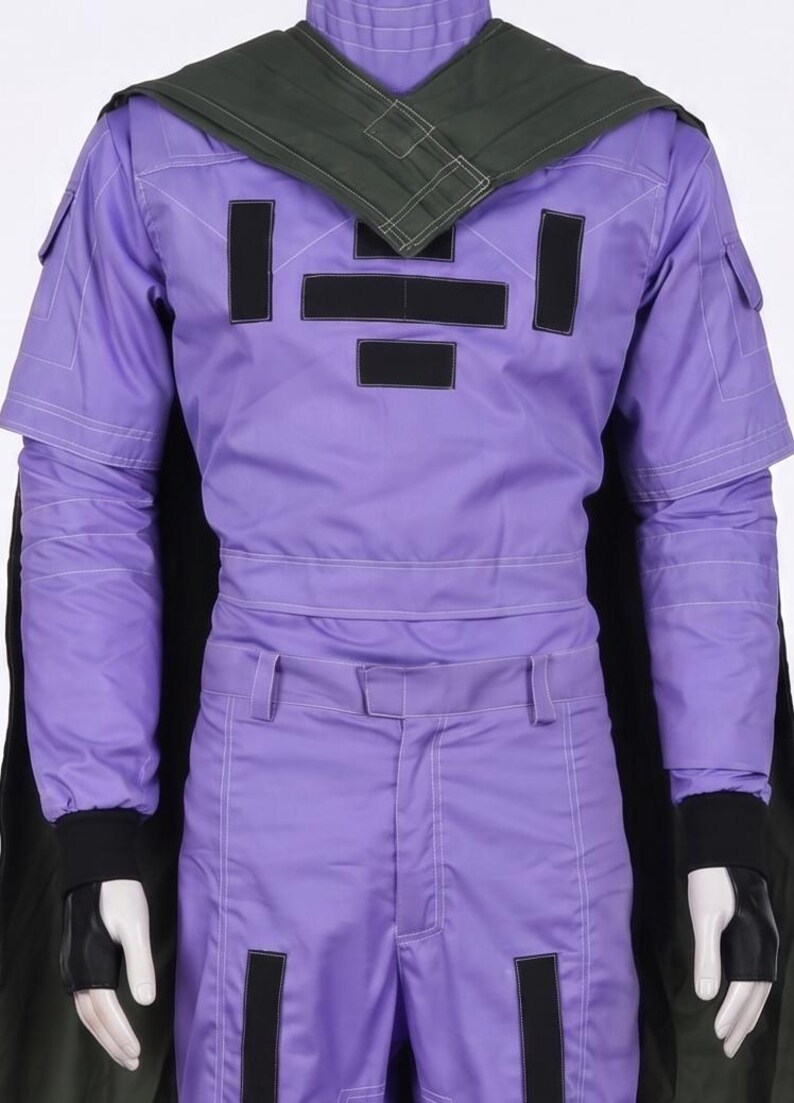 May include: A purple long-sleeved jumpsuit featuring a dark green cape, black rectangular patches on the chest and legs, and black fingerless gloves. The garment includes white topstitching details, a high collar, and utility-style pockets.