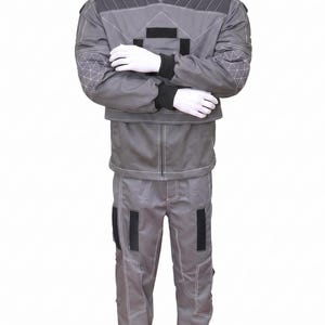 May include: A gray two-piece uniform set consisting of a long-sleeved jacket and matching trousers. The jacket features a high collar, dark gray shoulder panels with white stitching, and black rectangular accents. The sleeves have a geometric pattern.