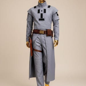 May include: A gray costume with a high collar, long sleeves, and a matching long coat. The outfit includes a brown belt with pouches, a holster, and gold-colored boots. The mannequin has a gold-colored head.