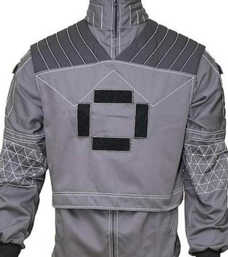 May include: A grey tactical-style jacket featuring a high collar, dark grey ribbed shoulder panels, and four rectangular black hook-and-loop patches on the chest. The sleeves display a white geometric grid pattern, and white contrast stitching.