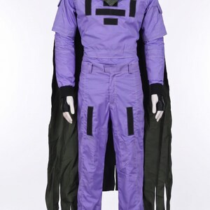 May include: A purple long-sleeved jumpsuit with a high collar, featuring black rectangular patches on the chest and thighs. A dark green cape is attached at the shoulders, and black fingerless gloves are worn on the hands of the white mannequin.