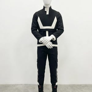 May include: A black long-sleeved jacket with a high collar and a white geometric chest design, paired with matching black cargo pants featuring white side stripes. The outfit includes white gloves and black high-top sneakers on a mannequin.
