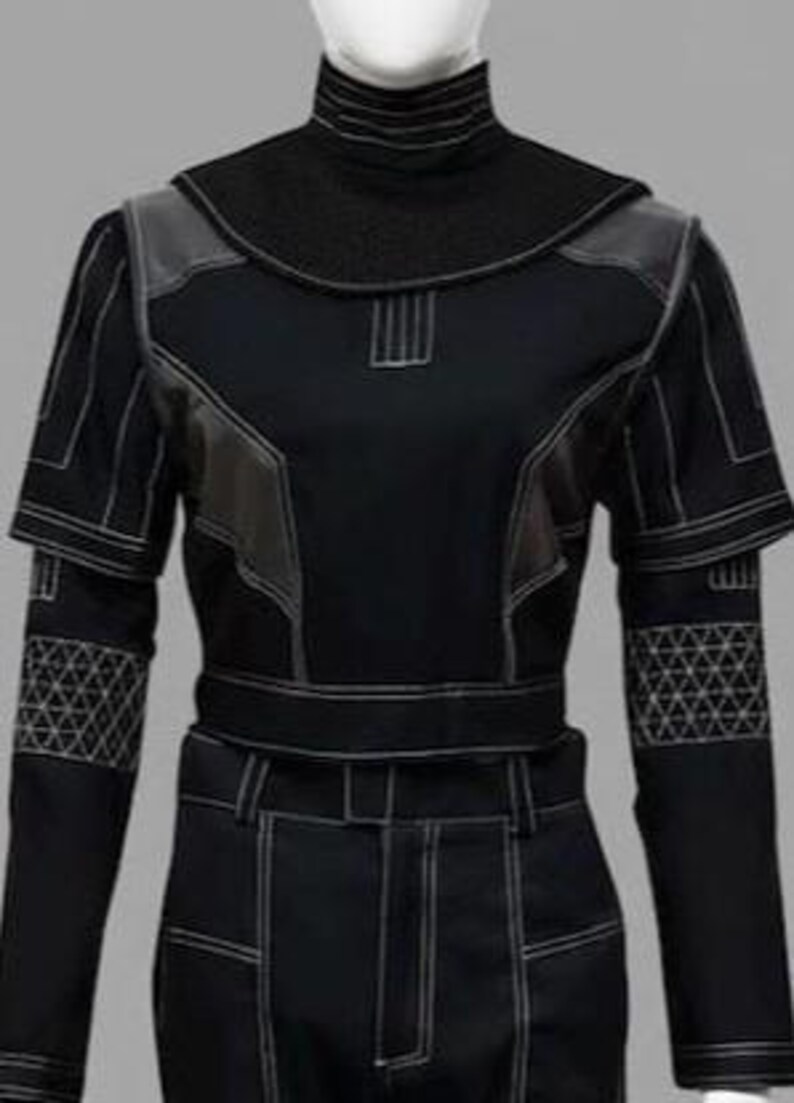 K&ouml;nnte beinhalten: Ein schwarzes Langarmshirt mit hohem Stehkragen, wei&szlig;en Kontrastn&auml;hten, strukturierten Schulterpartien und einem geometrischen Dreiecksgittermuster an den Unterarmen. Das Kleidungsst&uuml;ck ist bauchfrei geschnitten und hat eng anliegende &Auml;rmel.
