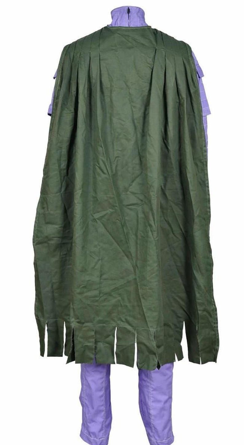 May include: A long, dark green cape with a pleated upper section and a fringed bottom edge, worn over a light purple garment with a high collar and visible vertical stitching details. The cape covers the back of the purple outfit completely.