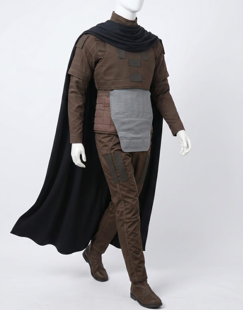 May include: A brown long-sleeved tunic with a high collar, a black cape, and matching brown trousers. The outfit includes a grey rectangular abdominal plate, a quilted brown waist section, and dark brown boots, all displayed on a white mannequin.