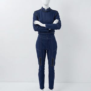 Op de afbeelding: Een donkerblauwe tweedelige outfit bestaande uit een top met lange mouwen met een hoge kraag en een bijpassende broek. De set is voorzien van opvallende witte contraststiksels, gestructureerde panelen en zwarte rechthoekige accenten op de bovenbenen.