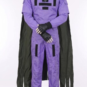 May include: A lavender jumpsuit with a high collar, short sleeves, and long pants. The garment features black rectangular patches on the chest and legs, a dark olive green cape draped over the shoulders, and black fingerless gloves on the hands.