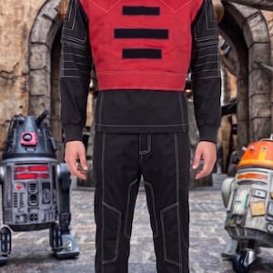 May include: A long-sleeved black shirt with a high neck and a red chest panel featuring three horizontal black rectangular patches. The shirt and matching black trousers are accented with prominent white topstitching throughout the garment.