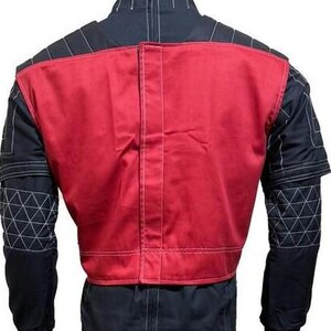 May include: A black jacket featuring a prominent red panel on the back, white contrast stitching throughout, and a geometric triangular pattern on the sleeves. The garment includes a vertical center seam and structured shoulder detailing.