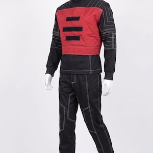 May include: A black long-sleeved shirt and matching pants set featuring white contrast stitching. The shirt includes a red chest panel with three horizontal black rectangular patches and a high collar. The outfit is displayed on a white mannequin.