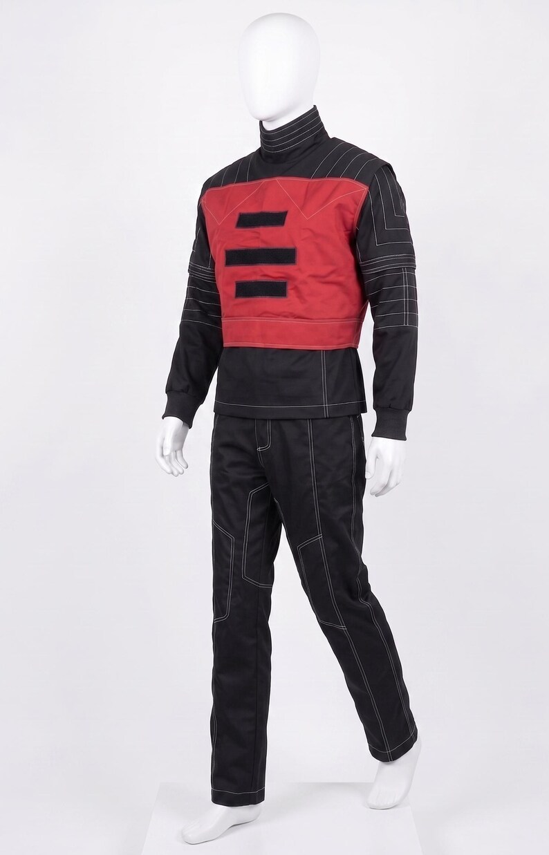 May include: A black long-sleeved shirt and matching pants set featuring white contrast stitching. The shirt includes a red chest panel with three horizontal black rectangular patches and a high collar. The outfit is displayed on a white mannequin.