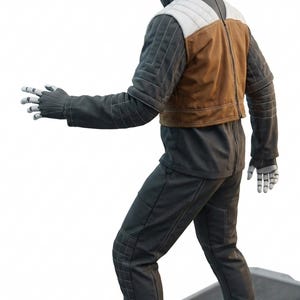 May include: A futuristic humanoid figure in a dark grey jumpsuit with white stitching, a brown vest, and white and grey padded shoulder detail. The figure has a pale face and hands, posed on a metallic platform.
