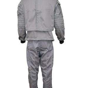 May include: A grey two-piece outfit consisting of a long-sleeved jacket and matching trousers. The jacket features a high collar, structured shoulder panels with horizontal stitching, and white contrast piping. The trousers have vertical seams.