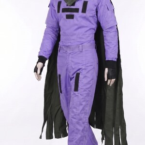 May include: A purple long-sleeved jumpsuit featuring a high collar, black rectangular chest patches, and black fingerless gloves. A dark olive green cape with a textured shoulder yoke and a fringed hem drapes over the shoulders of the mannequin.
