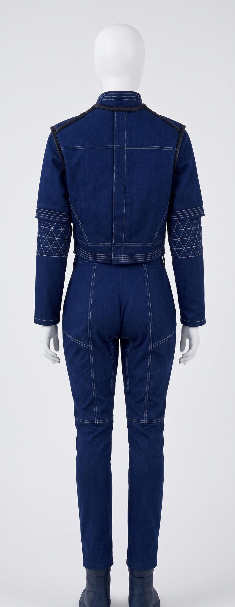 Op de afbeelding: Een donkerblauwe spijkerjumpsuit met een hoge kraag, lange mouwen met doorgestikte elleboogstukken en witte contraststiksels. Het kledingstuk heeft een aansluitend lijfje, een gedefinieerde taille en een broek met rechte pijpen.