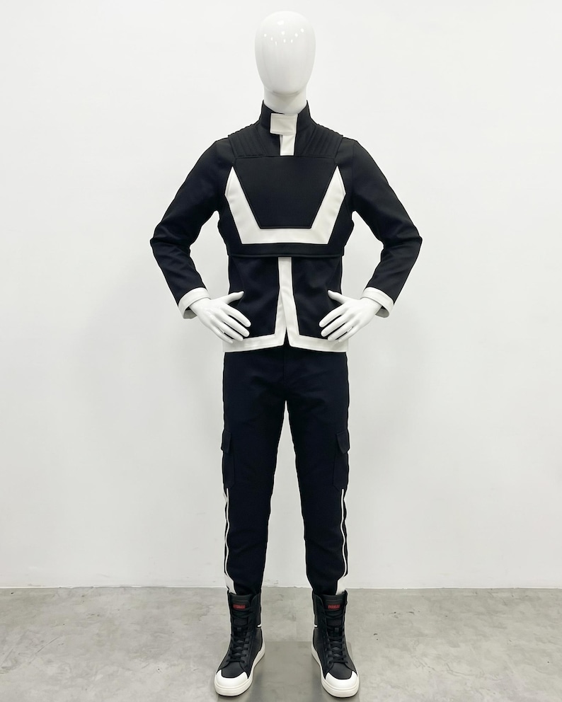 May include: A black and white long-sleeved jacket with a high collar and ribbed shoulder detailing, paired with matching black cargo-style trousers featuring white side stripes and black high-top sneakers worn on a white mannequin figure.