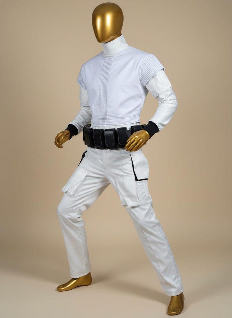 Pu&ograve; includere: Un costume bianco futuristico su un manichino. L'outfit include un top a collo alto con cuciture verticali, pantaloni abbinati con tasche cargo e una cintura nera con tasche. La testa e le mani del manichino sono dorate.