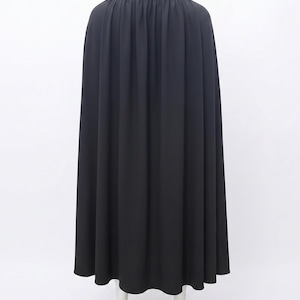 May include: A floor-length black cape featuring a high collar and gathered fabric at the neckline. The garment drapes down from the shoulders in vertical folds, creating a full silhouette that extends to the hemline, covering the back area.