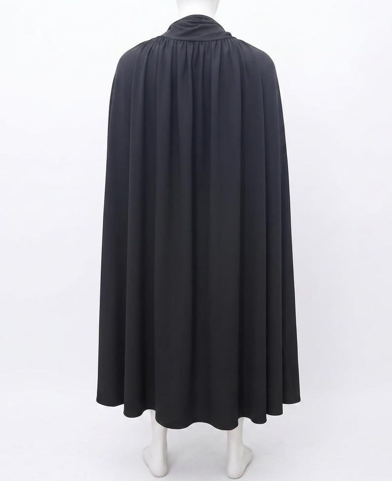 May include: A floor-length black cape featuring a high collar and gathered fabric at the neckline. The garment drapes down from the shoulders in vertical folds, creating a full silhouette that extends to the hemline, covering the back area.