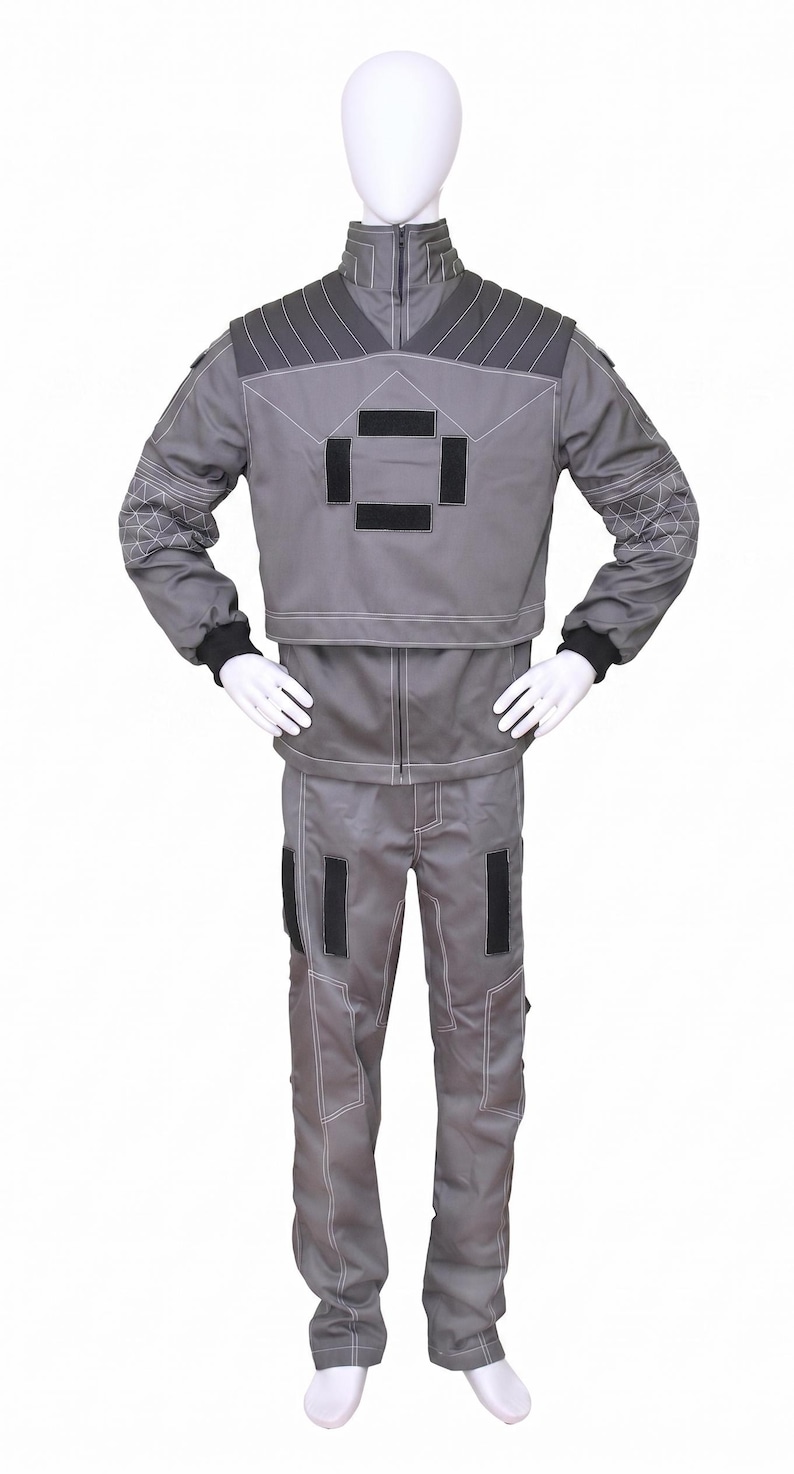 May include: A gray two-piece uniform set consisting of a long-sleeved jacket and matching trousers. The jacket features a high collar, dark gray shoulder panels, and a central square emblem made of four black rectangular patches with white stitching.