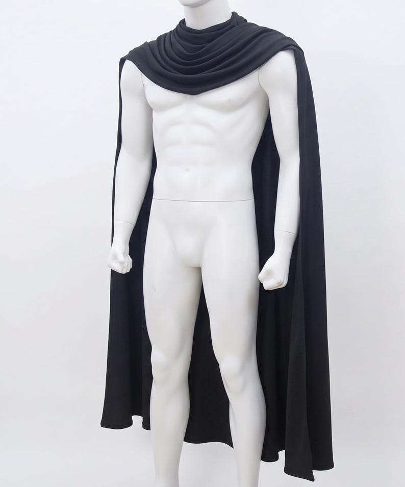 May include: A solid black cape featuring a draped, cowl-style neckline that rests around the shoulders. The fabric is smooth and opaque, extending down the back and sides in a long, flowing silhouette that reaches past the waistline.
