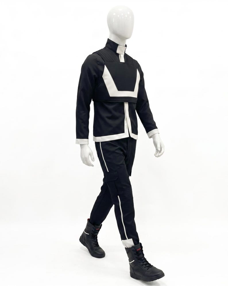 May include: A black long-sleeved jacket with a high collar and a white geometric chest panel, paired with matching black trousers featuring a white vertical stripe down the leg and black lace-up boots, displayed on a white mannequin.