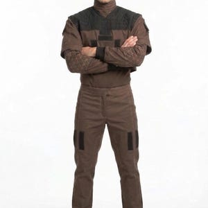 May include: A brown jumpsuit with a high collar and black accents. The outfit features diamond-patterned sleeves and black patches on the pants. The person is wearing black boots.