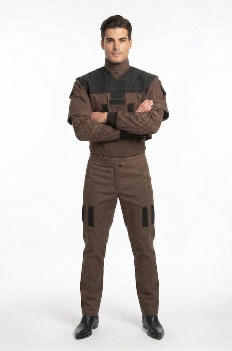 May include: A brown jumpsuit with a high collar and black accents. The outfit features diamond-patterned sleeves and black patches on the pants. The person is wearing black boots.