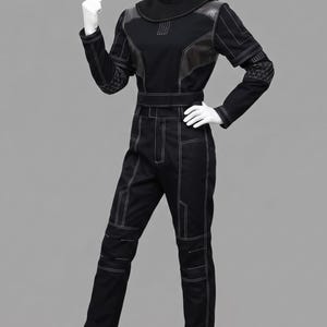 K&ouml;nnte beinhalten: Ein schwarzer Jumpsuit mit hohem Stehkragen, langen &Auml;rmeln und einer taillierten Passform. Das Kleidungsst&uuml;ck ist mit wei&szlig;en Kontrastn&auml;hten versehen, einschlie&szlig;lich geometrischer Muster an den &Auml;rmeln und Beinen sowie dunklen Schulterpartien.