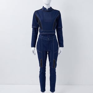 Op de afbeelding: Een donkerblauwe tweedelige outfit bestaande uit een top met lange mouwen en een hoge kraag, gecombineerd met een bijpassende slim-fit broek. De set is voorzien van opvallende witte stiksels, gestructureerde schouderpanelen en zwarte accenten.
