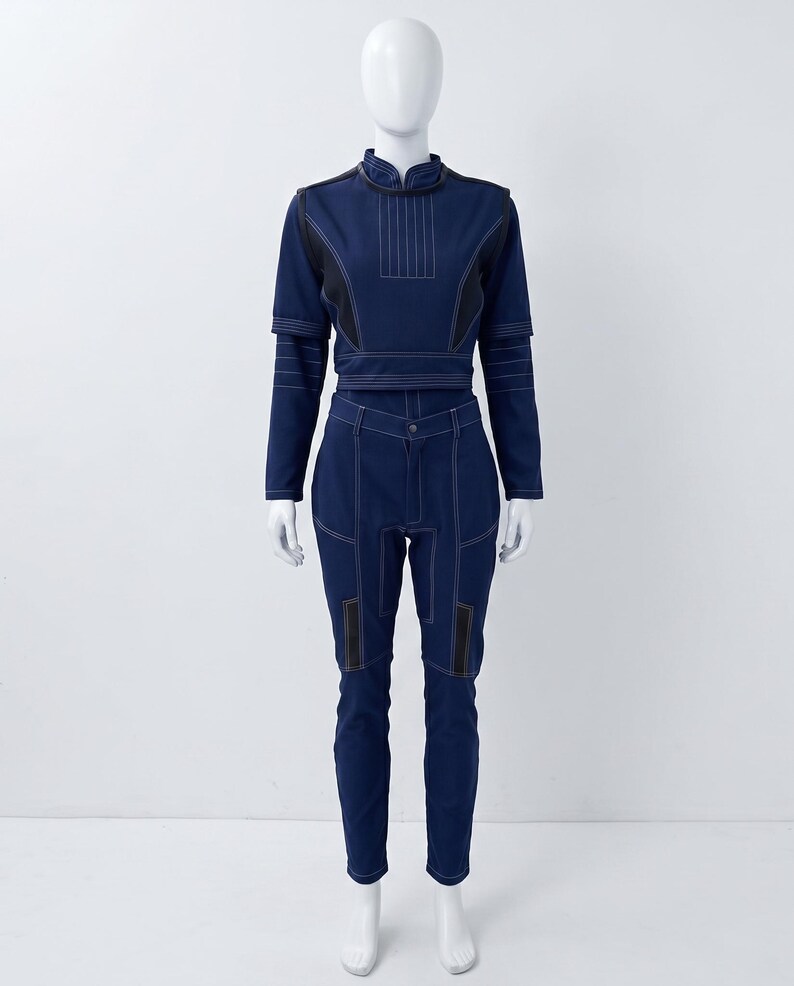 Op de afbeelding: Een donkerblauwe tweedelige outfit bestaande uit een top met lange mouwen en een hoge kraag, gecombineerd met een bijpassende slim-fit broek. De set is voorzien van opvallende witte stiksels, gestructureerde schouderpanelen en zwarte accenten.