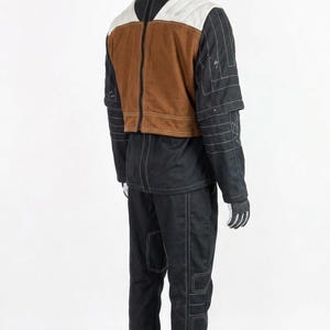 May include: A black and brown outfit with white stitching, displayed on a mannequin. The outfit includes a jacket with a brown vest, white shoulder accents, and black sleeves. Matching black trousers and gloves complete the ensemble. White shoes are worn.