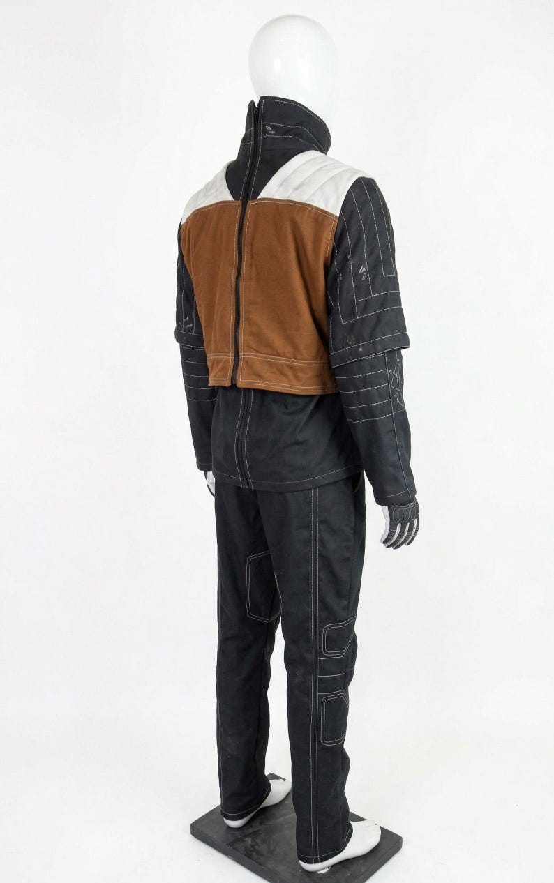 May include: A black and brown outfit with white stitching, displayed on a mannequin. The outfit includes a jacket with a brown vest, white shoulder accents, and black sleeves. Matching black trousers and gloves complete the ensemble. White shoes are worn.