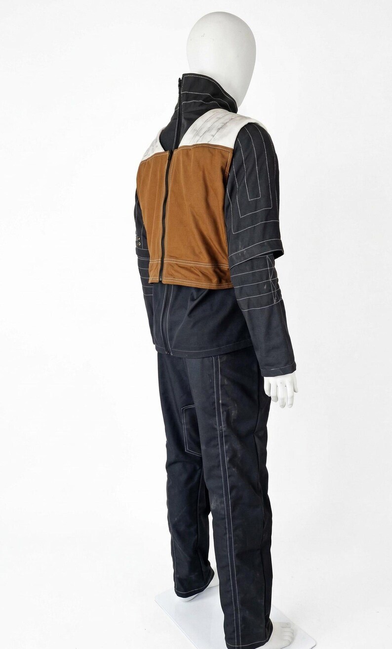 May include: A mannequin wearing a black and brown jacket and black trousers. The jacket has a brown torso, white shoulder accents, and black sleeves with white stitching. The trousers also have white stitching.