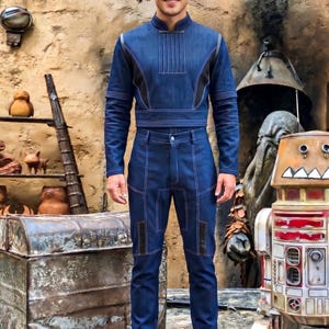 Op de afbeelding: Een donkerblauw denim shirt met lange mouwen, een hoge kraag en verticale stiksels, gecombineerd met een bijpassende donkerblauwe denim broek met verstevigde kniestukken en witte contraststiksels over het gehele tweedelige kostuum.
