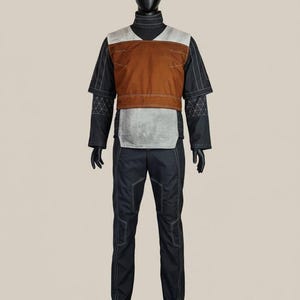 May include: A full outfit displayed on a mannequin. The outfit comprises a black turtleneck, a brown and grey vest, black trousers, and black gloves. White stitching highlights the seams. The mannequin stands on a grey base.