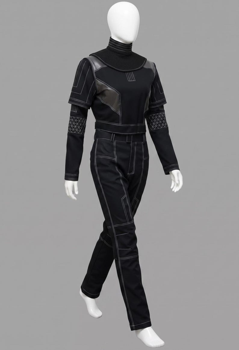 K&ouml;nnte beinhalten: Ein schwarzer Langarm-Jumpsuit mit hohem Stehkragen, kurz&auml;rmeligem &Uuml;berwurf und langer Hose. Das Kleidungsst&uuml;ck ist mit wei&szlig;en Kontrastn&auml;hten, geometrischen Mustern an den Unterarmen und dunkelgrauen Schulterpartien akzentuiert.