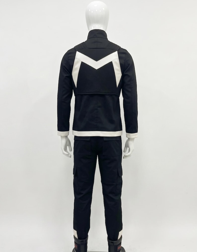 May include: A black jacket and matching trousers set featuring a white M-shaped emblem on the back of the jacket. The jacket has a high collar and white trim at the hem and cuffs. The trousers are long with side cargo pockets and white accents.