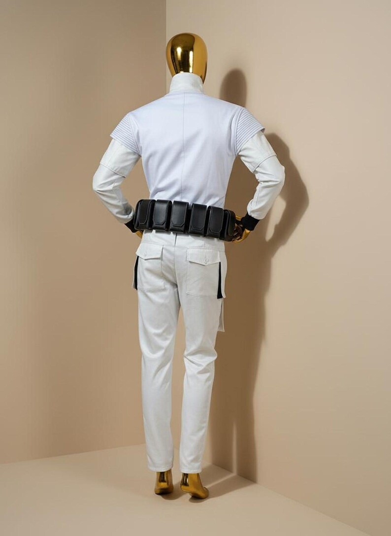 Pu&ograve; includere: Un costume bianco con collo alto, maniche lunghe e cintura nera con tasche. I pantaloni sono bianchi con dettagli neri. La testa e i piedi del manichino sono dorati.