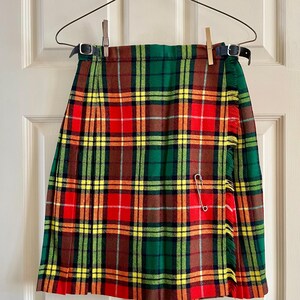 Peut inclure: Un kilt à carreaux coloré aux tons rouge, vert, jaune et marron, suspendu à un cintre métallique. Le kilt présente un motif plissé et est fixé avec une épingle de sûreté. Le kilt est maintenu par deux pinces à linge.