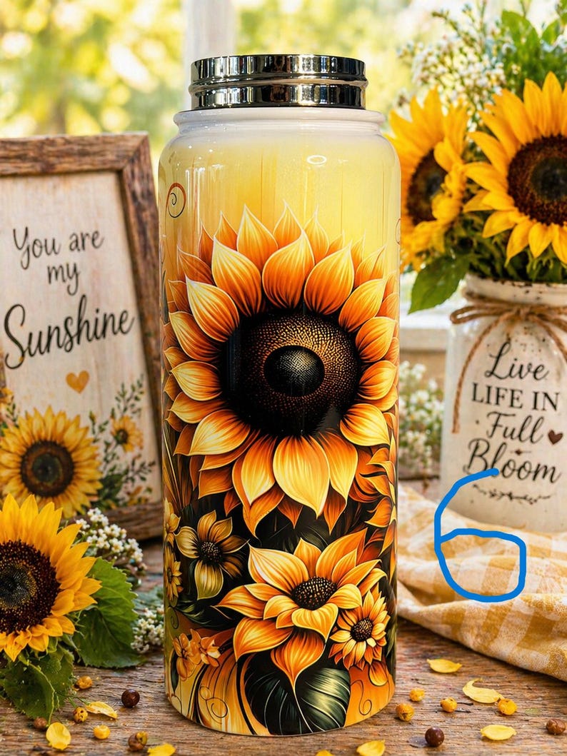 May include: A stainless steel water bottle with a vibrant sunflower design. The bottle features a large, detailed sunflower in shades of yellow, orange, and brown. The background is a gradient of yellow. The bottle has a silver lid and is surrounded by sunflowers.