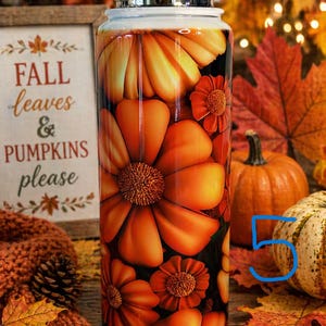 May include: A stainless steel water bottle with a floral design in shades of orange and yellow. The bottle features large, stylized flowers and smaller blossoms. The words "FALL leaves & PUMPKINS please" are visible on a wooden sign.