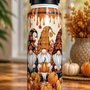 May include: A stainless steel water bottle featuring a fall-themed design. The bottle showcases three gnomes holding pumpkins, surrounded by autumn leaves and pumpkins. The top has a black handle and lid.