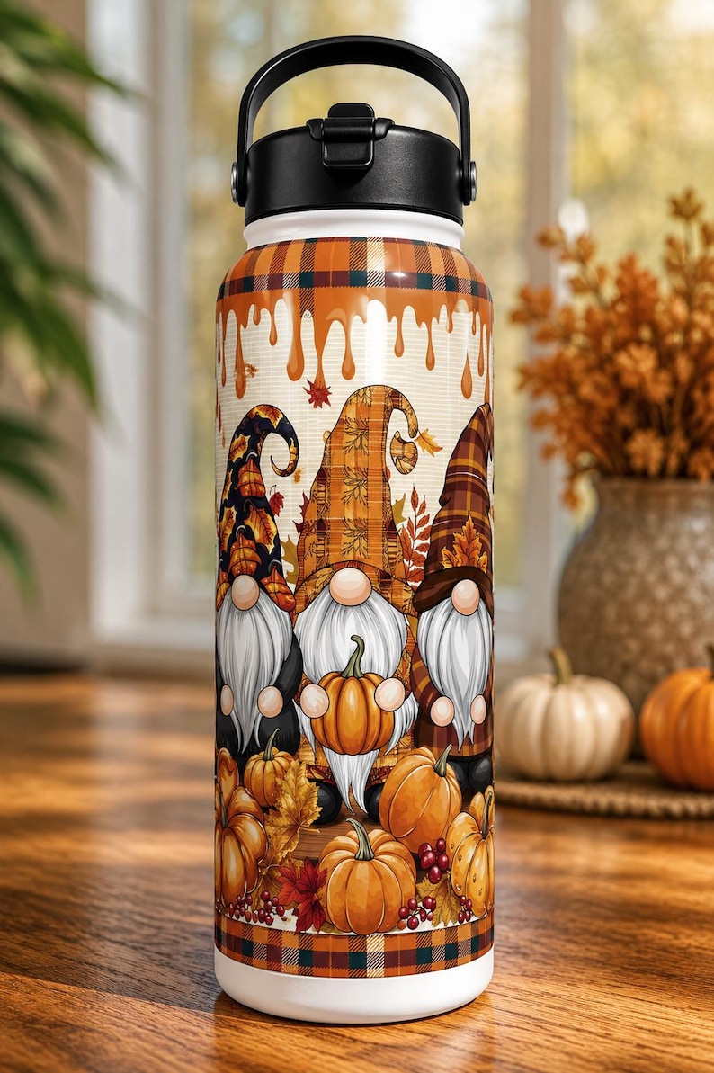 May include: A stainless steel water bottle featuring a fall-themed design. The bottle showcases three gnomes holding pumpkins, surrounded by autumn leaves and pumpkins. The top has a black handle and lid.