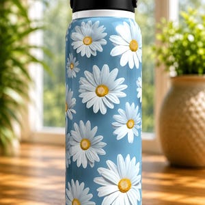 K&ouml;nnte beinhalten: Eine Edelstahl-Wasserflasche mit hellblauem Hintergrund und einem Muster aus wei&szlig;en G&auml;nsebl&uuml;mchen mit gelben Zentren. Die Flasche hat einen schwarzen Griff und Deckel sowie einen wei&szlig;en Boden. Ideal f&uuml;r die Fl&uuml;ssigkeitszufuhr.