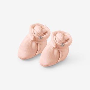 Puede incluir: Un par de botines de bebé de color rosa pálido. Los botines tienen una puntera redondeada y un puño doblado. La tela tiene una sutil textura acanalada. Una pequeña etiqueta está cosida en el puño. Los botines están diseñados para mantener calientes los pies del bebé.